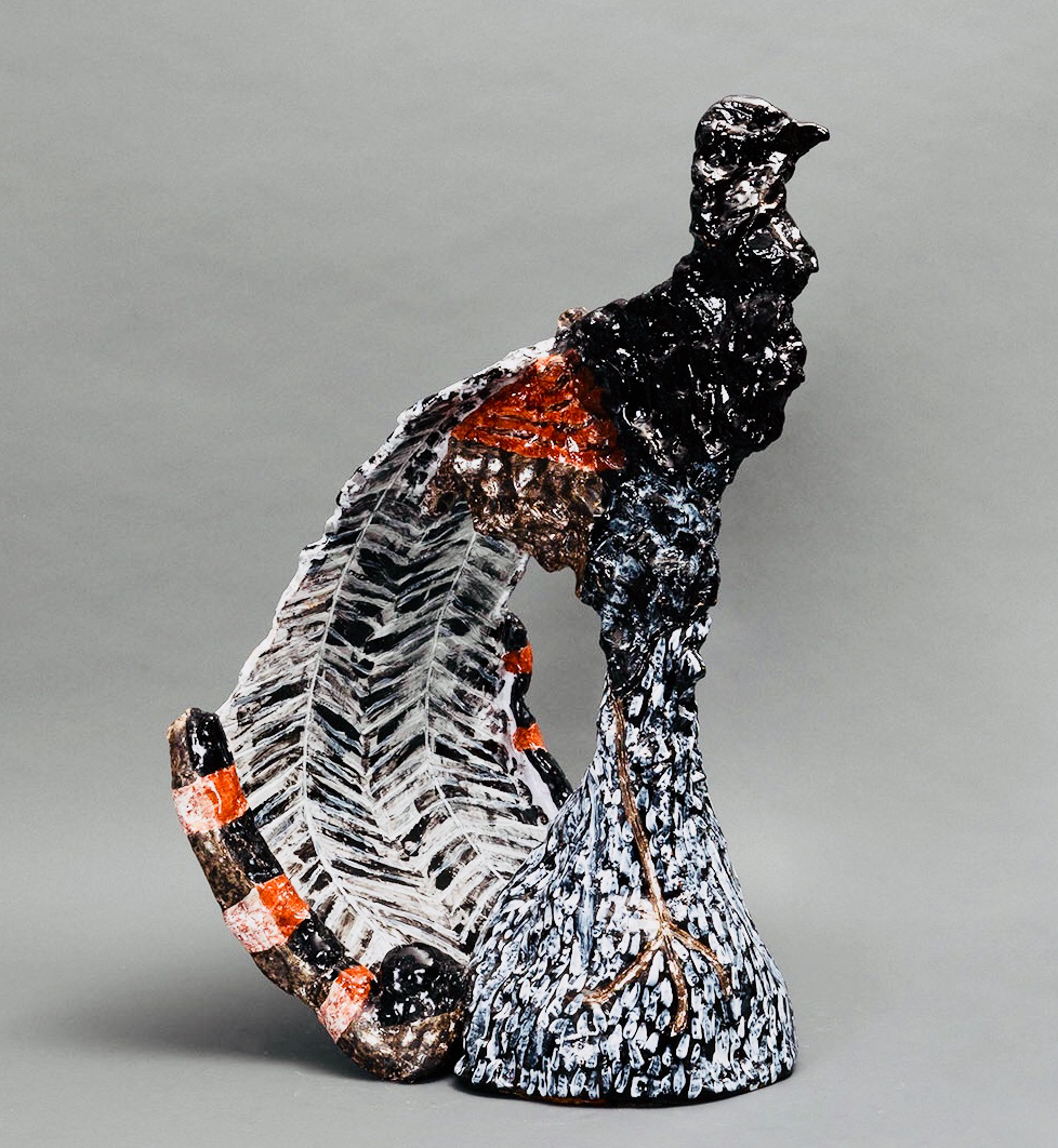 Alt text: Ceramic sculpture of a stylised male lyrebird in black, red, brown and white. The lyrebird stands erect on a mound of earth with its lyre-shaped feathered tail lowered and curved behind it. 